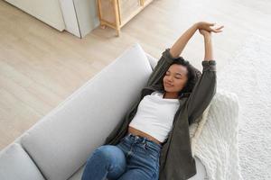 Serene african american girl napping, relaxing lying on comfortable sofa at home, stretching arms photo