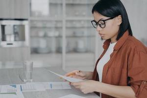 Focused businesswoman analyzing documents with statistics, working on financial project on workspace photo