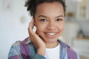 Smiling mixed race young girl using modern earphone listen to music or answer video call, head shot photo