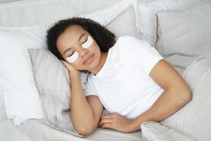 Una joven mestiza dormida con parches debajo de los ojos en la cara se relaja, acostada en la cama. rutina de cuidado de la piel foto