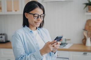 Happy female uses mobile phone apps, shopping in online store, checking social networks at home photo