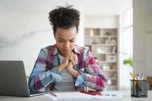 Mixed race girl student solves task, preparing for exam at desk with laptop. Stress and education photo
