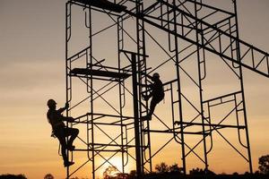 teamwork construction worker installation scaffolding in industrial construction sunset sky background overtime job Silhouette. photo