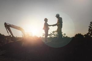 apretón de manos de ingeniero y trabajador en la silueta del sitio de construcción foto