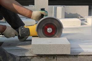 manos de trabajador con amoladora eléctrica recorta losas de pavimentación en el sitio de construcción. concepto de colocación de nuevas baldosas en la acera. equipo de corte de piedra. obras viales Ingeniería civil. reparar asfalto. de cerca foto