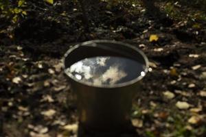 Water in bucket. Steel bucket in garden. Reflection of sun in water for watering plants. photo