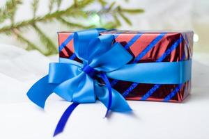 A Christmas gift decorated with a beautiful bow on a light background with a twig, if. Selective focus. the concept of Christmas and New Year. photo