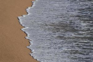 Foam from the waves as they reach the sand on the beach photo