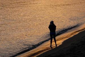 retroiluminación de una silueta de una mujer anónima tomando fotos en el mar