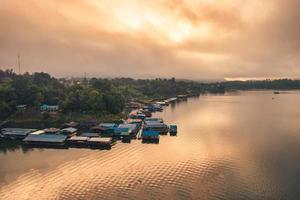 Golden sunrise over local traditional Mon village floating with foggy in the dam at the morning in Sangkhlaburi photo