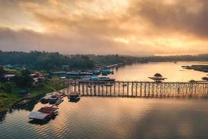 Golden sunrise over Mon wooden bridge on Songkalia river and Mon local village at Sangkhlaburi photo