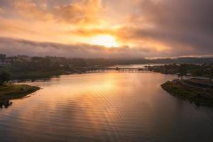 Golden sunrise over Mon wooden bridge on Songkalia river and Mon local village at Sangkhlaburi photo