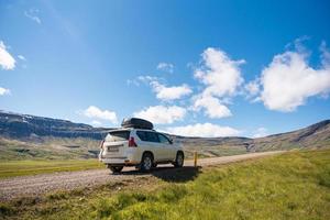 Large car parked on dirt road among the mountain and meadow on sunny day in summer photo
