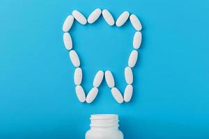 White Vitamins with calcium Ca, D3 in the form of a tooth scattered from a white jar on a blue background photo