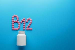 Pink pills in the shape of the letter B12 on a blue background, spilled out of a white can. photo