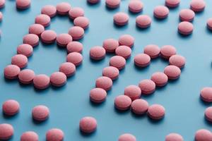 Pink tablets in the form of B12 in the heart on a blue background, spilled from a white can. photo