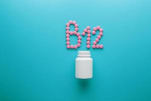 Pink pills in the shape of the letter B12 on a blue background, spilled out of a white can. photo