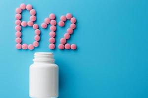 Pink pills in the shape of the letter B12 on a blue background, spilled out of a white can. photo