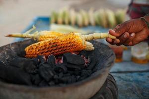 Close-up hands of female street vendor is rubbing a roasted sweet corn cob with lemon and spices. Indian street food concept, closeup photo