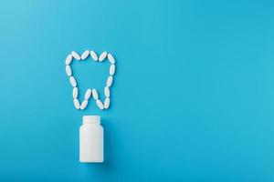 Vitamins with calcium in the form of a tooth spilled out of a white jar on a blue background. Pharmaceuticals and dentistry, dental care