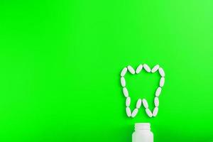 Calcium vitamin in the form of a tooth spilled out of a white jar on a Green background. photo