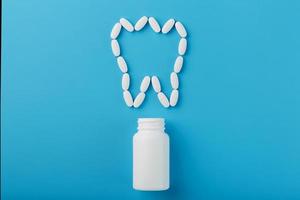 Tooth made of white vitamins with calcium on a blue background. Vitamins spilled out of a tooth-shaped jar. Ca, D3. photo