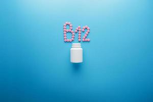 pastillas rosas en forma de letra b12 sobre un fondo azul, derramadas de una lata blanca. foto