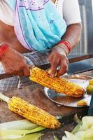 Close-up hands of female street vendor is rubbing a roasted sweet corn cob with lemon and spices. Indian street food concept, closeup photo