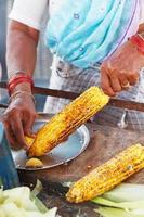 Close-up hands of female street vendor is rubbing a roasted sweet corn cob with lemon and spices. Indian street food concept, closeup photo