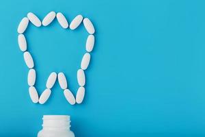 Vitamins with calcium in the form of a tooth spilled out of a white jar on a blue background. Pharmaceuticals and dentistry, dental care