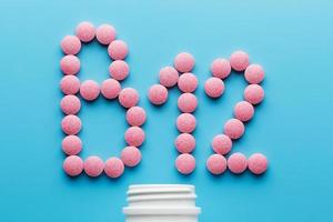 Pink pills in the shape of the letter B12 on a blue background, spilled out of a white can. photo