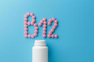 Pink pills in the shape of the letter B12 on a blue background, spilled out of a white can. photo