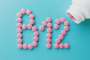 Pink tablets in the form of B12 close-up on a blue background from a white can, low contrast photo