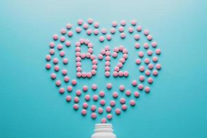 Pink tablets in the form of B12 in the heart on a blue background, spilled from a white can low contrast photo