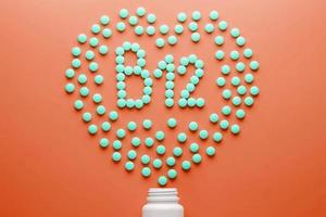 Vitamins B 12 in the shape of a heart on a red substrate, poured out of a white jar. photo