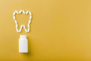 Calcium vitamin in the form of a tooth spilled out of a white jar on a yellow background. photo