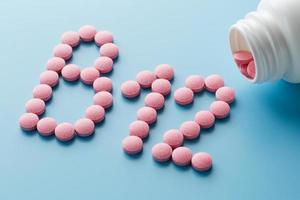 Pink round vitamins B12 shaped pills on a blue background spilled from a white can photo