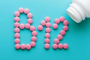 Pink pills in the shape of the letter B12 on a blue background, spilled out of a white can. photo