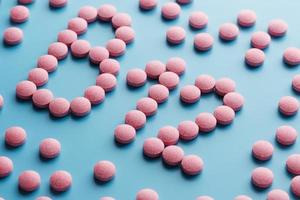 Pink pills in the shape of the letter B12 on a blue background, spilled out of a white can. photo