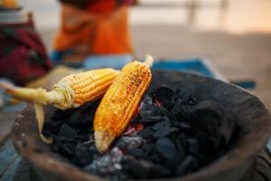 mazorcas de maíz dorado sobre las brasas en la parrilla. en la playa de arambol al atardecer. asiático, comida callejera india foto