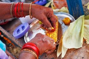 Close-up hands of female street vendor is rubbing a roasted sweet corn cob with lemon and spices. Indian street food concept, closeup photo