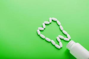 vitamina de calcio en forma de diente derramado de un frasco blanco sobre un fondo verde. foto