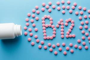 Pink pills in the shape of the letter B12 on a blue background, spilled out of a white can. photo