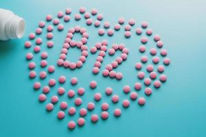 Pink tablets in the form of B12 in the heart on a blue background, spilled from a white can low contrast photo