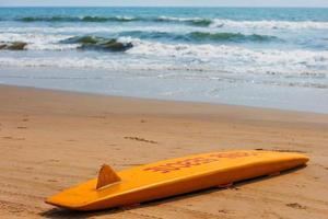 The yellow board of the rescuer for surfing lies on the sand used by the lifeguard working on the Arambol beach photo