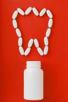 Calcium vitamin in the form of a tooth spilled out of a white jar on a red background.
