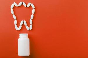 Calcium vitamin in the form of a tooth spilled out of a white jar on a red background.
