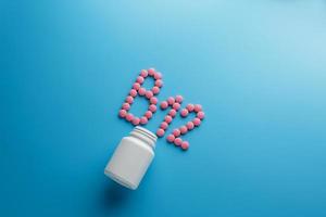 Pink pills in the shape of the letter B12 on a blue background, spilled out of a white can. photo