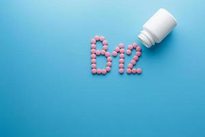 Pink pills in the shape of the letter B12 on a blue background, spilled out of a white can. photo