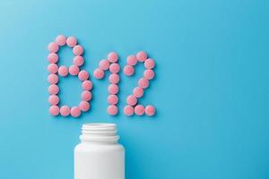 píldoras redondas rosadas con forma de vitaminas b12 sobre un fondo azul derramadas de una lata blanca foto